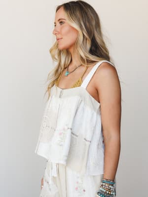 A breezy patchwork woven tank top in natural white layered over a mustard lace camisole, styled with stacked beaded bracelets and a turquoise pendant necklace — effortlessly boho and made for warm-weather wandering.