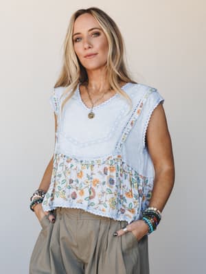 A relaxed, layered boho top in baby blue with a floral peplum hem and lace trim, styled with wide-leg olive trousers and stacked beaded bracelets — the kind of outfit that looks effortless but is clearly very much on purpose.