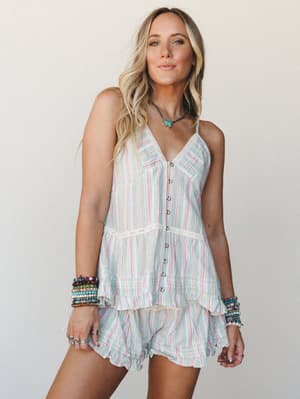 A breezy striped matching set — cami top and ruffle shorts — styled with stacked beaded bracelets and a turquoise pendant necklace, giving off effortless summer energy against a soft neutral studio wall.