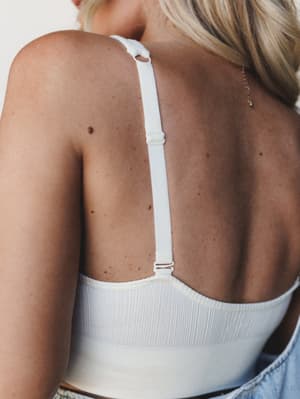 A close-up back shot showing the adjustable single-strap detail of a ribbed ivory bralette, styled with denim — clean, effortless, and very much the kind of piece you forget you're wearing.
