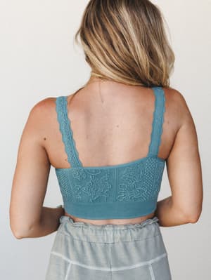 A back-facing shot of a textured teal bralette with floral jacquard detailing and scalloped lace straps, paired with a washed sage tiered skirt — soft, relaxed, and quietly pretty.