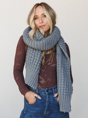 A relaxed, effortlessly layered look — chunky slate blue-gray wrap scarf draped over a burgundy star-print long-sleeve top and denim, the kind of outfit that looks like you just threw it on and somehow nailed it.