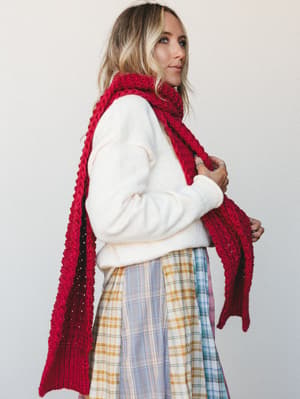 A cream sweater and plaid midi skirt layered with an oversized chunky knit scarf in raspberry red — the kind of cozy-meets-put-together outfit that makes a Tuesday feel intentional.