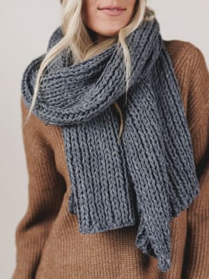 Person wearing a large knitted scarf and brown sweater against a neutral background