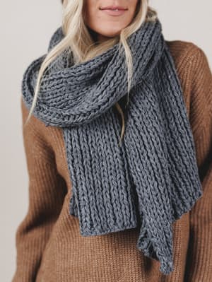 Person wearing a large knitted scarf and brown sweater against a neutral background