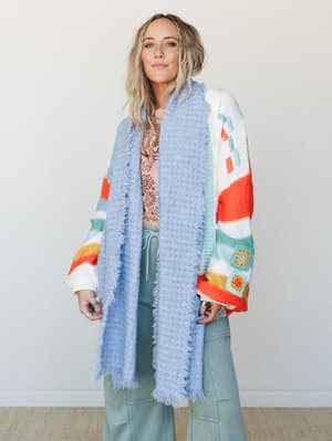 A breezy layered look built around a soft periwinkle waffle-knit scarf with fringe edges, worn over a colorblock crochet cardigan and wide-leg sage pants — the kind of outfit that looks like it came together effortlessly but absolutely did not.