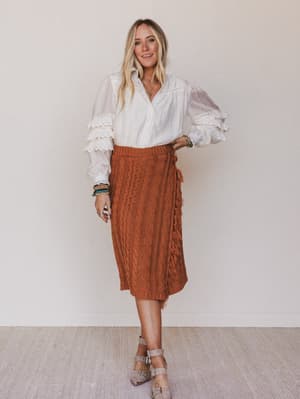Woman wearing a white blouse and brown skirt against a plain background