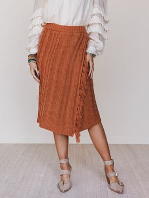 Person wearing a rust-colored knitted skirt with a plain background