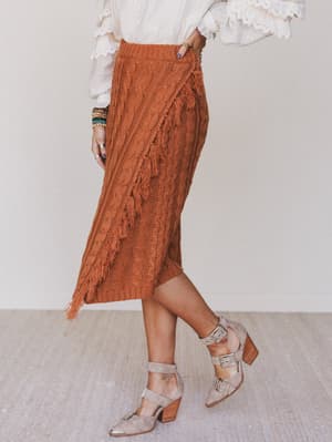 Person wearing a rust-colored lace skirt with a white blouse and beige sandals on a neutral background