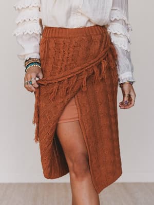 Person wearing a brown knitted skirt with tassels on a plain background