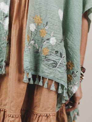 Green embroidered garment with tassels and floral patterns on a neutral background