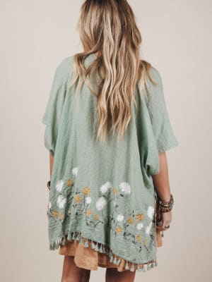 Person wearing a green embroidered dress with floral patterns on a plain background