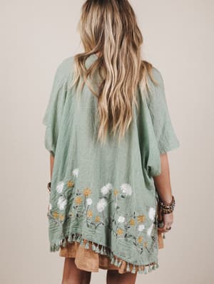 Person wearing a green embroidered dress with floral patterns on a plain background
