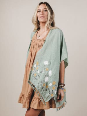 Woman wearing a green floral poncho over a brown dress on a beige background