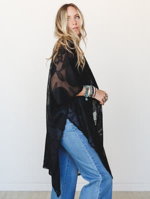 A sheer black lace kimono worn over wide-leg light-wash jeans, styled with a stack of turquoise and earth-tone beaded bracelets — the kind of outfit that feels effortless and a little mysterious at the same time.