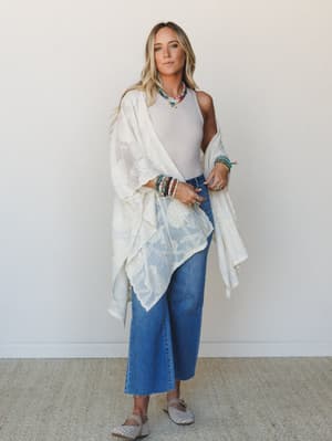 A relaxed full-body shot of a model in a flowy cream lace kimono layered over a white tank and wide-leg cropped jeans, styled with stacked beaded bracelets and a colorful layered necklace — the kind of effortless outfit that looks like it came togeth
