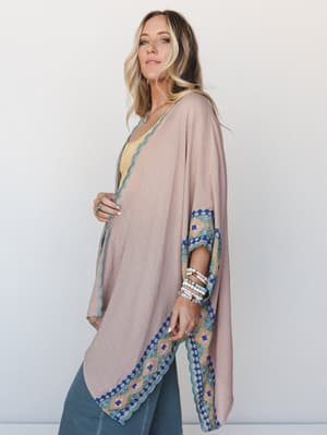 A flowy clay-toned kimono with vibrant embroidered border trim along the hem and sleeves, layered over a yellow cami and jeans — the kind of piece that makes a casual outfit feel completely intentional.