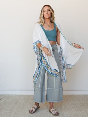 A breezy ivory kimono with colorful embroidered border trim layered over a dusty teal crochet crop top and wide-leg cropped pants — the kind of outfit that looks effortless but was absolutely thought about.