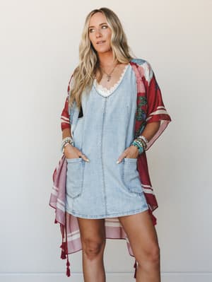 A breezy, effortlessly layered look — a light wash denim mini dress peeking out beneath a flowy floral kimono in deep burgundy, styled with stacked turquoise bracelets and a delicate pendant necklace for that perfect boho-casual mix.