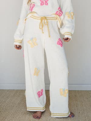 A cream knit wide-leg pant set covered in pastel crochet butterfly appliqués — the kind of outfit that makes you want to stay in it all day but still looks like you tried.