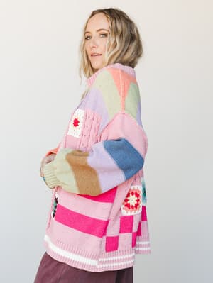 A colorblock knit cardigan with granny square crochet patches worn by a model in a three-quarter side pose — playful, cozy, and the kind of piece that looks like it came from your most fun friend's closet.