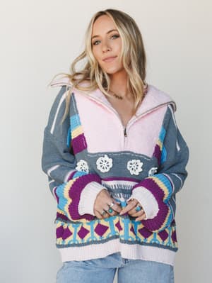 A colorful, chunky knit pullover with a fleece-lined half-zip collar gets the full boho-cozy treatment — layered with silver rings and a gold necklace, it's the kind of sweater that makes a Tuesday feel like a creative decision.
