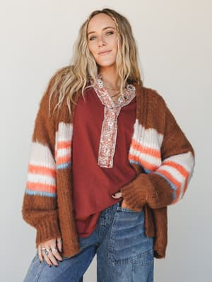 A cozy, oversized striped cardigan in warm caramel brown layered over a rust henley and wide-leg denim — the kind of outfit that looks like it came together effortlessly on a cool fall morning.