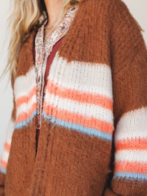 A close-up of a cozy, fuzzy striped cardigan in warm brick brown layered over a floral button-down — the kind of effortless layering combination that makes a Tuesday feel intentional.