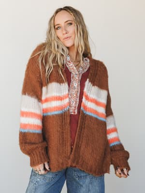 A fuzzy, oversized striped cardigan in warm caramel brown layered over a floral button-up and burgundy top with denim — the kind of effortless autumn outfit that looks like it came together by happy accident.