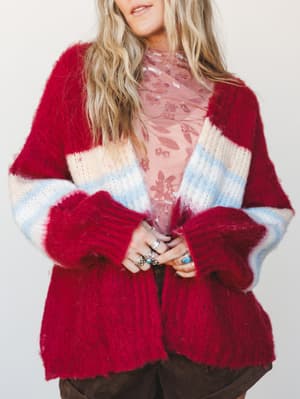 A cozy, oversized striped cardigan in cranberry, cream, and sky blue layered over a blush floral top — the kind of outfit that looks like it happened naturally but somehow gets compliments all day.