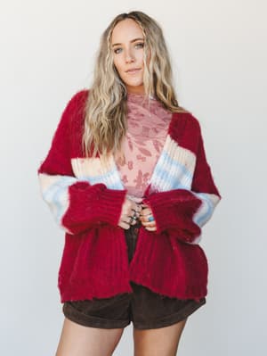 A chunky striped cardigan in cranberry red layered over a floral pink top with brown shorts — the kind of thrown-on-perfectly outfit that looks effortless but clearly wasn't accidental.