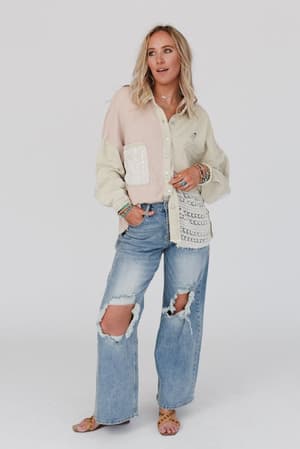 A woman with long blonde hair wears the Way Home Patch Detail Shacket in beige, paired with ripped light blue jeans, sandals, and colorful bracelets, standing against a plain white background.