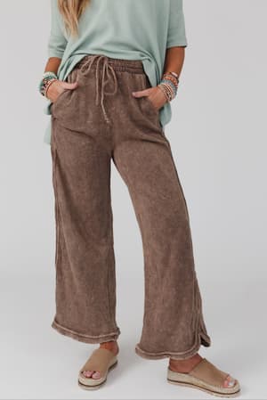 A person models the So Comfy Wide Leg Pant Full Length in Mocha, standing with hands in pockets. Only their lower torso, legs, and arms are visible against a plain background.