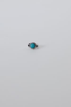The Kapalua Bay Adjustable Turquoise Ring in silver, featuring a round turquoise stone at the center, rests on a light gray surface—an elegant piece for any jewelry collection.