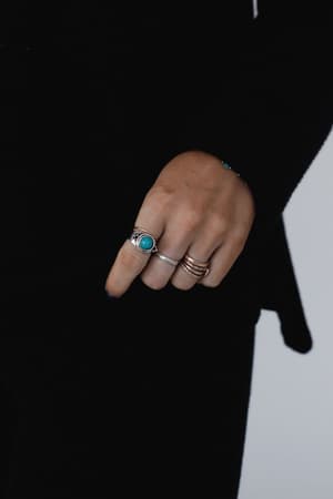 A hand adorned with the Kapalua Bay Adjustable Turquoise Ring - Silver, styled with boho jewelry, is shown against a dark long-sleeved top; the fingers are gently curled and the background is plain.