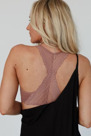A woman with long blonde hair is shown from the back, wearing the Evermore Seamless Lace Racerback Bralette in mauve under a draped black off-shoulder top, highlighting this stylish layering piece.