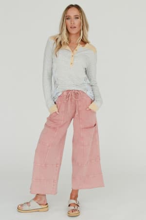 A woman with long blonde hair poses against a plain background wearing the Lucky One Wide Leg Pant in mauve, a long-sleeve striped knit shirt with beige accents, and beige sandals.