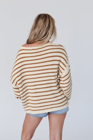 A person with long, blonde hair stands with their back to the camera against a plain light background, wearing the All My Stripes Oversized Sweater in mustard and denim shorts.