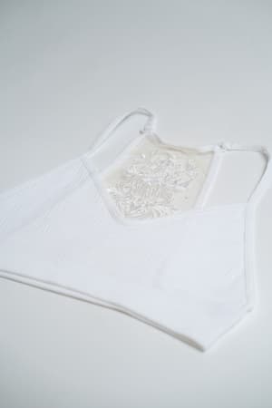 The Tattoo Bralette - White is a sleeveless crop top with thin straps and an embroidered mesh panel with delicate floral details, shown laid flat on a white background.