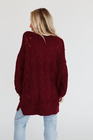 A woman with long blonde hair faces away, wearing the Golden Hour Bubble Sleeve Sweater Dress in burgundy against a plain white background.