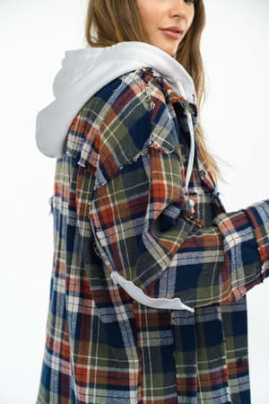 A person wearing the Flannel Layers Hooded Jacket - Navy Multi, featuring a white hood and an oversized green, navy, red, and cream plaid design with frayed seams, is shown in profile against a plain white background.