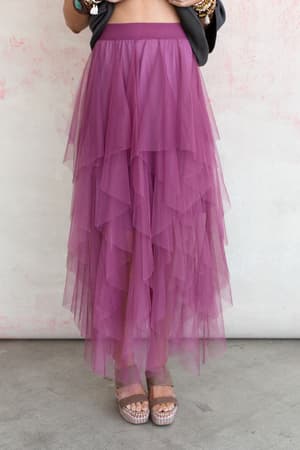 Standing against a light pink textured background, a person wears the Boho Ballerina Skirt - Mauve paired with metallic platform sandals. Their torso and face are not visible.