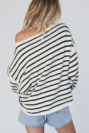 A woman with blonde hair, seen from behind, wears the All My Stripes Oversized Sweater - Cream Black off one shoulder with light denim shorts against a plain light background.