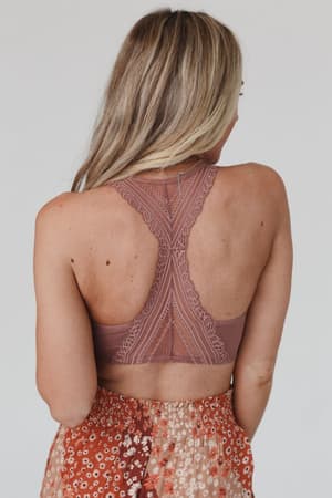 A woman with long blonde hair is seen from behind, wearing the Evermore Seamless Lace Racerback Bralette in mauve and a floral skirt, standing against a plain light background.