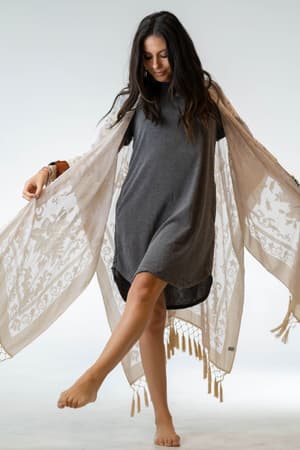 A woman with long dark hair, barefoot in a loose grey dress, poses gracefully against a plain background while wearing the Crushin' On You Velvet Kimono in nude.