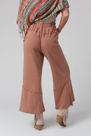 Model wears the Feeling Good Wide Leg Pant in Faded Rust, heeled ankle boots with fringe, and a multicolored striped shawl. Photo is taken from the back against a plain gray background.
