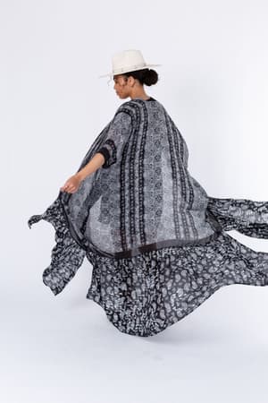 A person wearing the Paisley Tapestry Free Flow Duster Kimono in black is spinning, making the kimono flare out. They pair it with a white hat and are photographed against a plain white background.