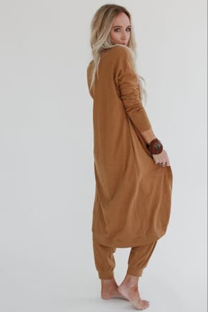 A woman with long blonde hair stands barefoot, looking over her shoulder in the Set to Go Textured Jumpsuit and Cardigan Set - Camel. She wears a large bracelet against a plain white background.