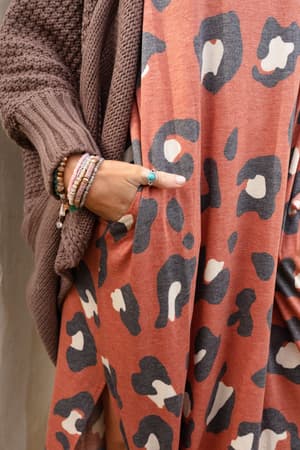 A person wearing a brown knit cardigan and an orange leopard-print dress showcases the Kapalua Bay Adjustable Turquoise Ring – Silver and beaded bracelets, with one hand in a pocket against a neutral background.