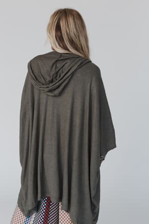 A person with long, light brown hair is shown from behind, wearing The Nest Boho Essential Hooded Ribbed Sweater in Olive and a red, blue, and white patterned skirt. The effortlessly stylish look stands out against a plain, light background.